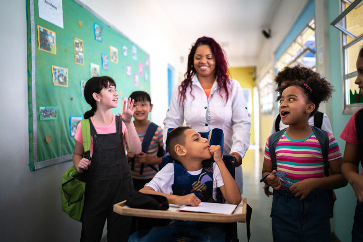 school counselor pushing boy in a wheelchair, surrounded by other students